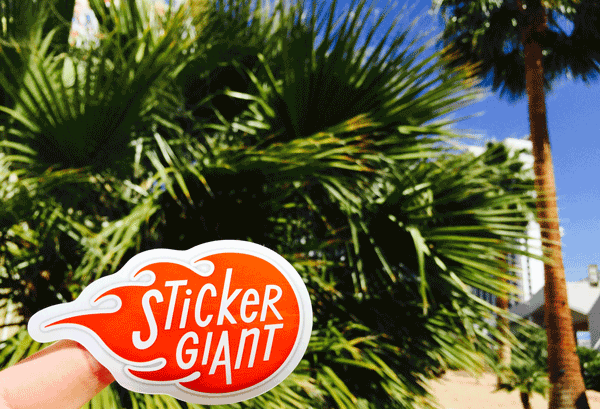 Sticker-Story-Day-celebrated-by-StickerGiant-with-logo-sticker-in-front-of-palm-trees